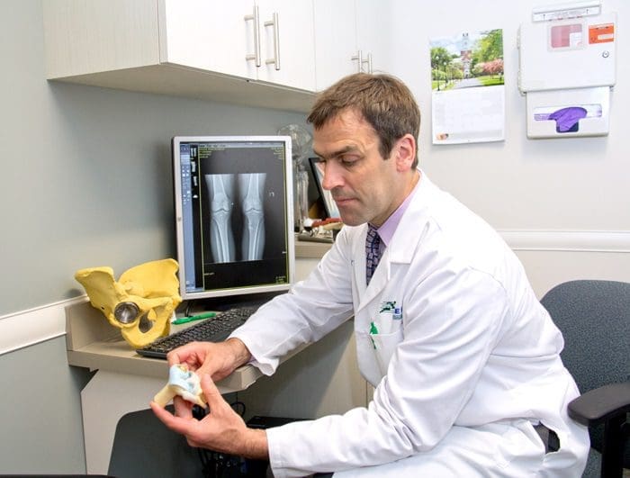 Dr. Fehm in an exam room showing an x-ray and bone models